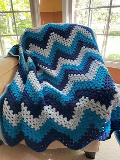 a blue and white crocheted blanket sitting on top of a couch next to a window