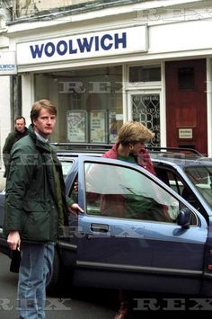 two people standing in front of a car talking on the phone while another person walks by