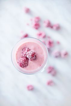 a smoothie with raspberries in it on a white surface surrounded by scattered berries