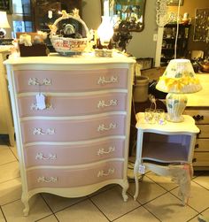 a pink dresser sitting on top of a tiled floor next to a table with a lamp