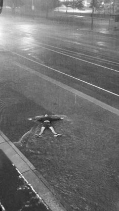 a black and white photo of a person laying on the ground in the rain with an umbrella over their head