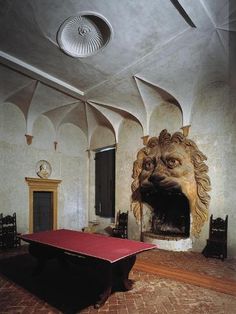 a room with a table and a lion head on the wall next to a fire place