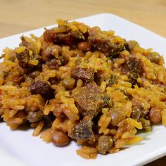 a white plate topped with rice and meat on top of a wooden table next to a fork