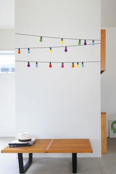 a wooden bench sitting in front of a white wall with colorful lights on the strings