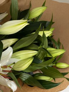 a bunch of white flowers sitting on top of a brown paper bag with green leaves