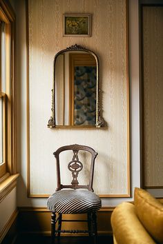 a chair sitting in front of a mirror next to a wall with a painting on it