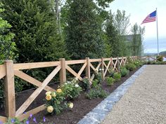 a wooden fence surrounded by flowers next to a gravel path with an american flag in the background