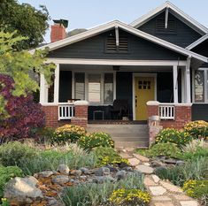 a black house with yellow door and flowers in the front yard on a sunny day