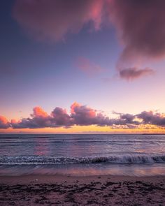 the sun is setting over the ocean with clouds in the sky and waves on the beach