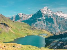 the mountains are covered in snow and green grass, with a lake surrounded by grassy hills