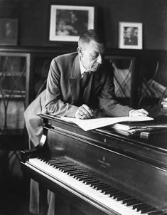 a man sitting at a piano writing on a piece of paper in front of him