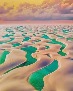 an aerial view of the water and sand dunes at sunset, with clouds in the sky