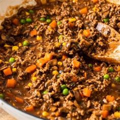 a large pot filled with meat and vegetables on top of a wooden table next to a spoon