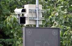 a security camera mounted to the side of a pole next to a sign with trees in the background