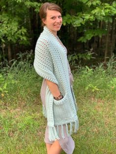 a woman standing in the grass wearing a crocheted shawl with fringes