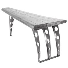 a metal bench sitting on top of a white surface with holes in the back ground