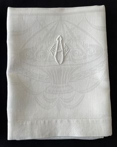 a white napkin with an embroidered monogram on the front and bottom, sitting on a black surface