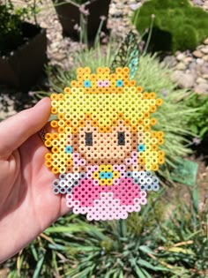 someone is holding up a small pixel art piece in their hand, with plants behind it