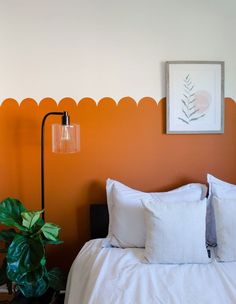 a bedroom with an orange wall and white bedding, potted plant in the corner