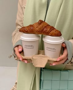 a woman holding two cups of coffee and a croissant