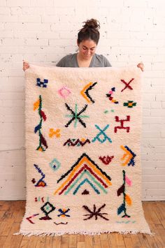 a woman holding up a large rug with colorful designs on it