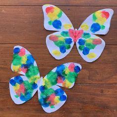 three paper butterflies are sitting on a wooden surface, one is multicolored and the other is white