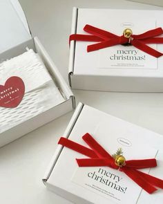 two white boxes with red ribbon and gold bells on them, one has a heart shaped ornament