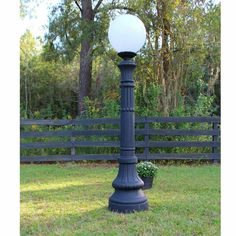 a lamp post sitting in the grass near a fence