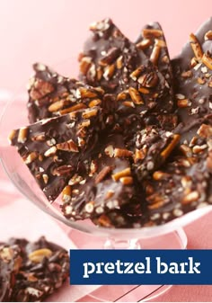 there are many pieces of chocolate with nuts in the glass bowl on the table and pink background