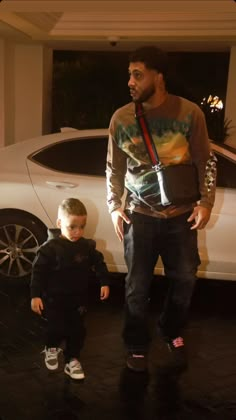 a man standing next to a little boy in front of a car