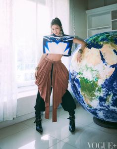 a woman standing in front of a window next to a large earth globe with her hands on her hips