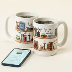 two coffee mugs sitting next to each other on a table with a cell phone