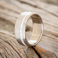 a wedding ring with white wood inlays sits on a wooden surface