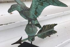 a metal bird sculpture sitting on top of a wooden table next to a window sill