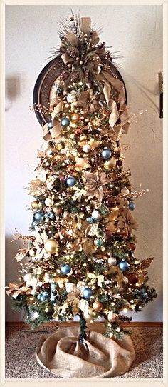 a decorated christmas tree with blue and gold ornaments on it's base, in front of a wall