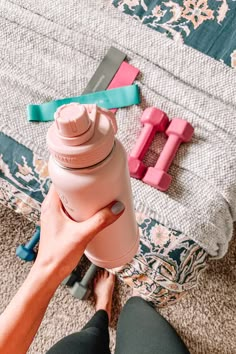 a person holding a pink water bottle in their hand next to other items on the floor