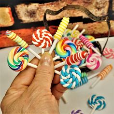 a hand is holding several lollipops in front of a pile of other lollipops