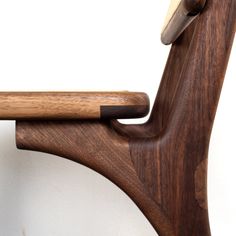 a close up of a wooden chair against a white wall with a wood handle on it