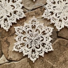 two white lace snowflakes sitting on top of a stone floor next to each other