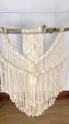 a white macrame hanging from a wooden pole in a room with wood flooring