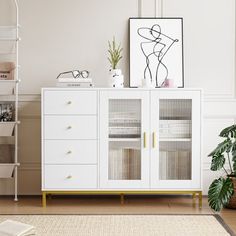 a white cabinet with glass doors and gold handles next to a potted plant on top of a rug