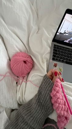 a person laying in bed next to a laptop computer with yarn on top of it