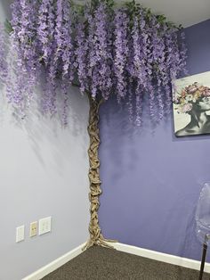 a tree with purple flowers is in the corner of a room