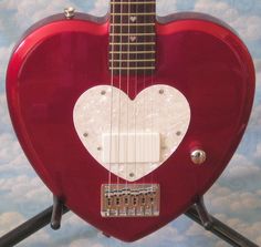 a red guitar with a white heart on it's back and neck, sitting on a stand