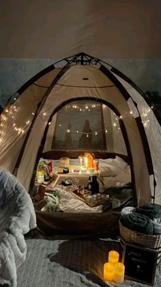 the inside of a tent is lit up with fairy lights and blankets on the floor