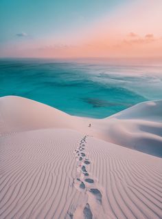 footprints in the sand at sunset with an ocean and sky behind it, as seen from above