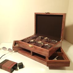 an open wooden box with many different items in it on a white surface next to some glasses