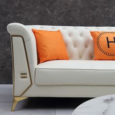 a white couch with two orange pillows on top of it and a coffee table in front of it