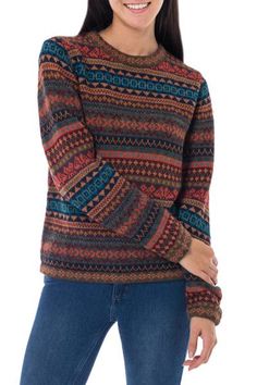 a woman is smiling and wearing a sweater with an intricate pattern on the front, she has her hands in her pockets