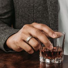 a man is holding his wedding ring while sitting at a table with a glass of whiskey